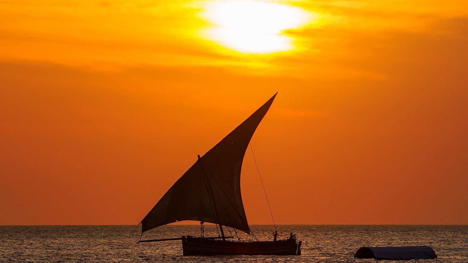 Een dhow-zeilboot bij zonsondergang voor de kust van Zanzibar