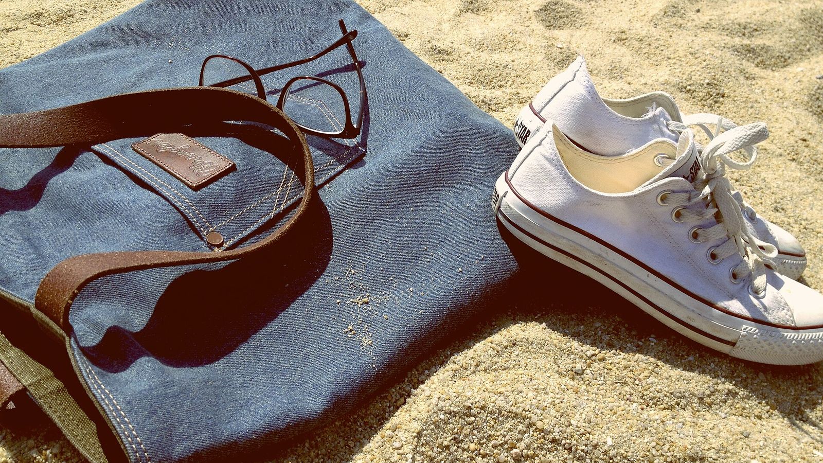 Strandtas, zonnebril en schoenen in het zand